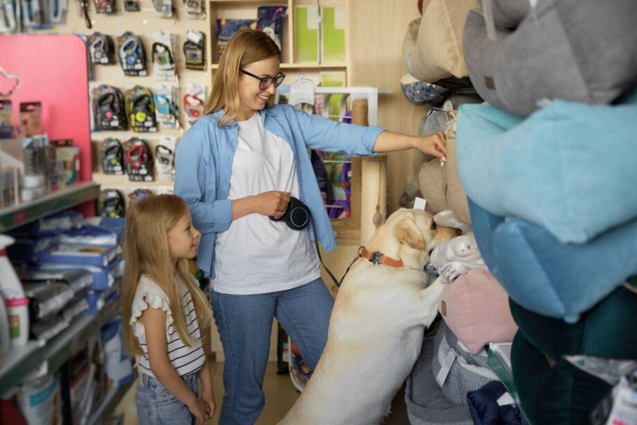 Kobieta z dziewczynką i psem oglądają produkty w sklepie zoologicznym.
